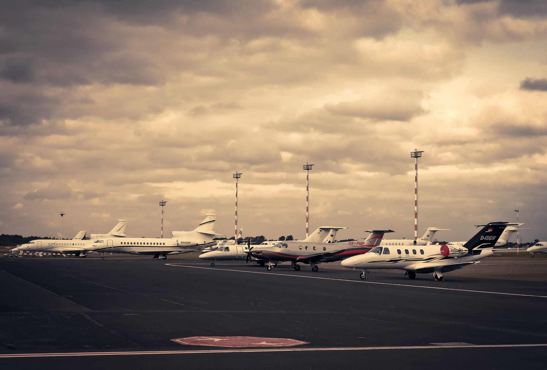 A row of business jets parked on a metro airport ramp under a dramatic sky