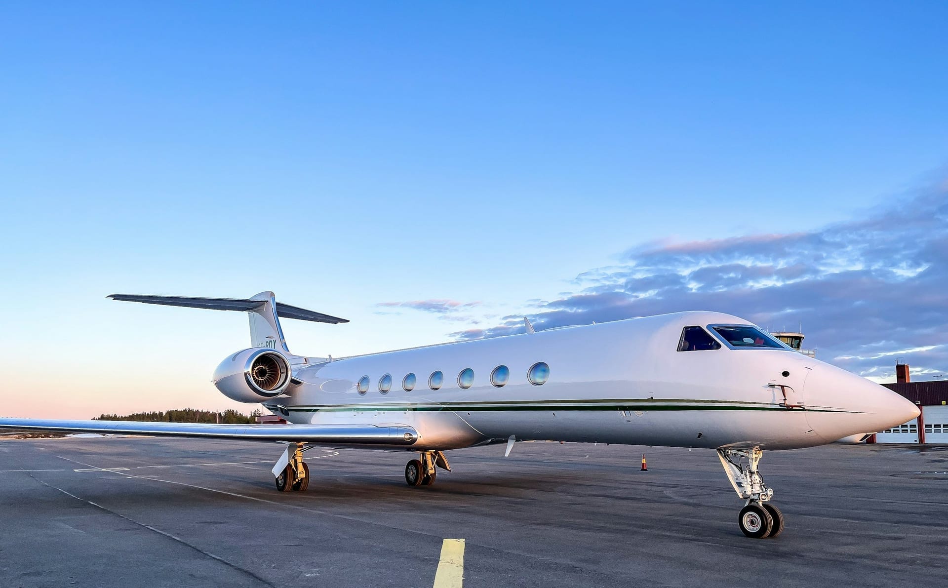 Business jet parked on an empty apron at dusk, with a control tower and airport buildings behind it