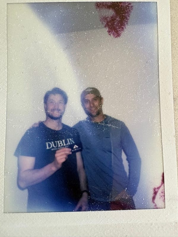 A Polaroid photograph resting on a counter, showing two members of the AirPlx team standing together, one holding an AirPlx sticker